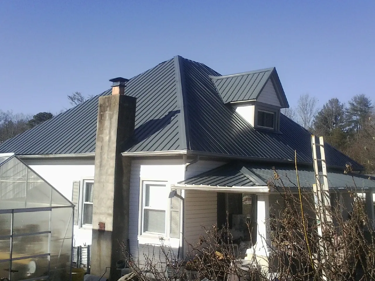 Dark blue standing seam metal roof on a white farmhouse with dormer — Slate & Tile Roof Repair by Roofing Brothers in Arvada