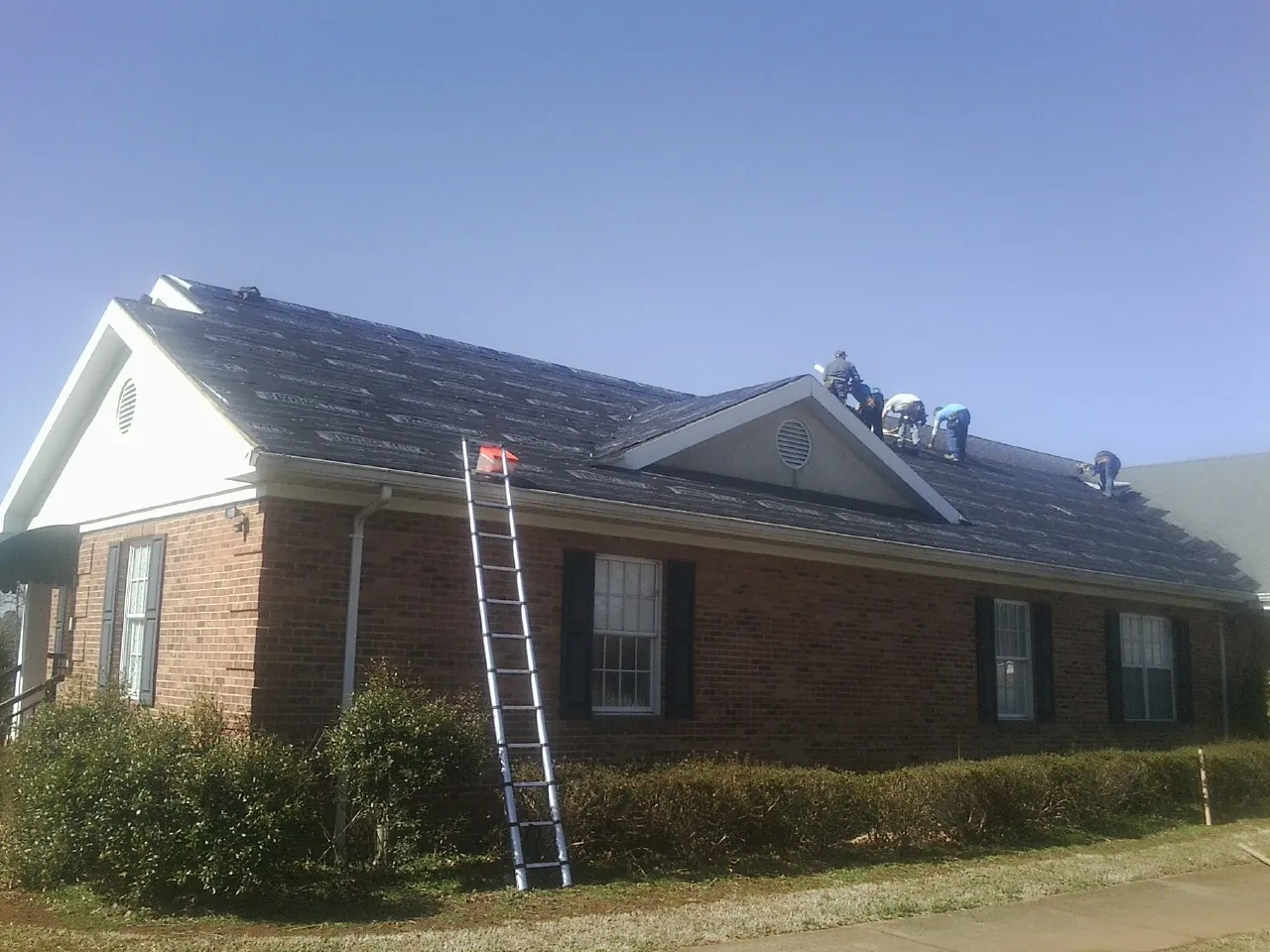 Crew tearing shingles off a brick ranch roof with a ladder set — Emergency Roof Repair work by our crew in Arvada