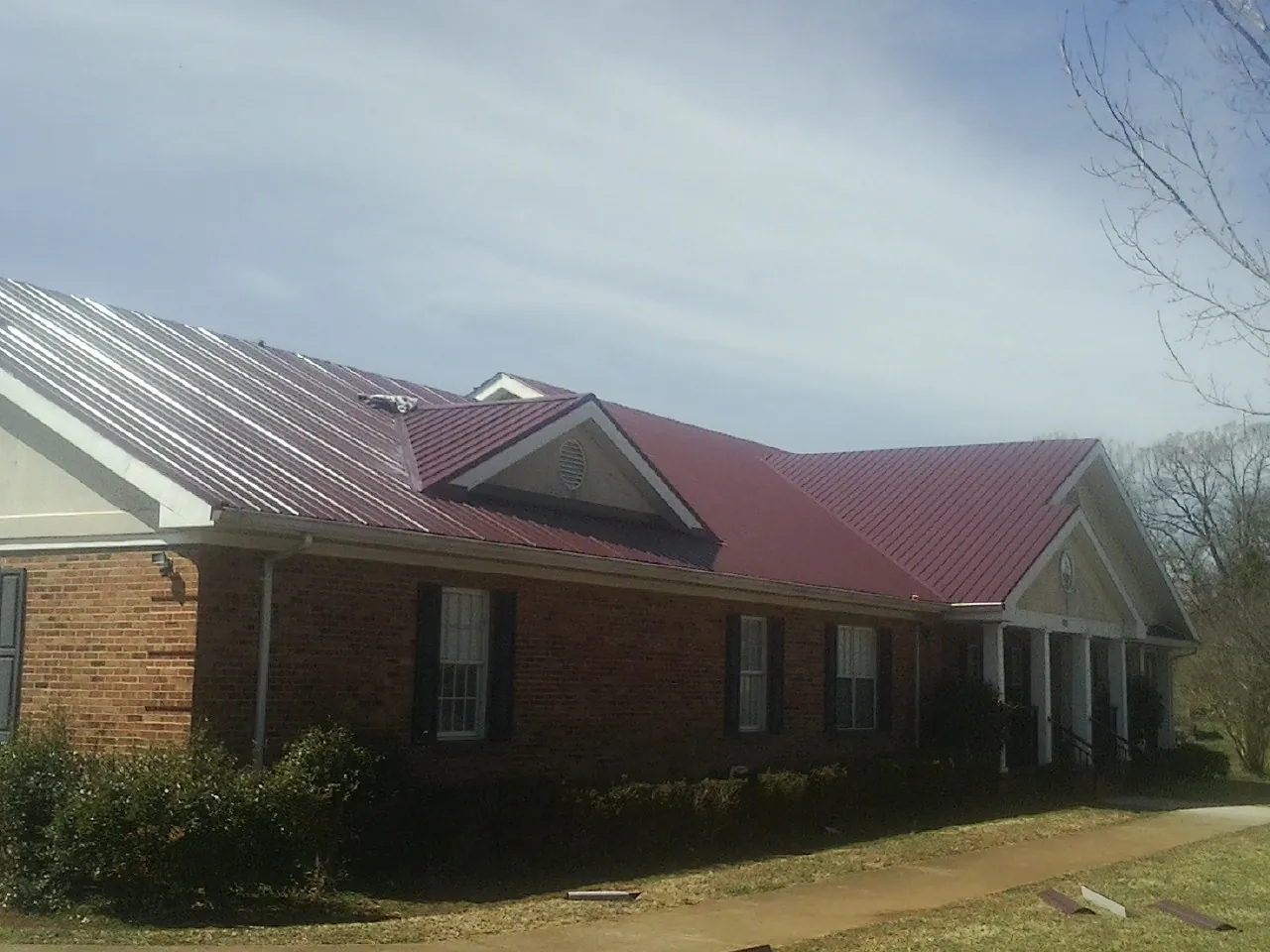 Red metal roof with gabled entries on a long brick building, from a Hail Damage Roof Repair job in Arvada