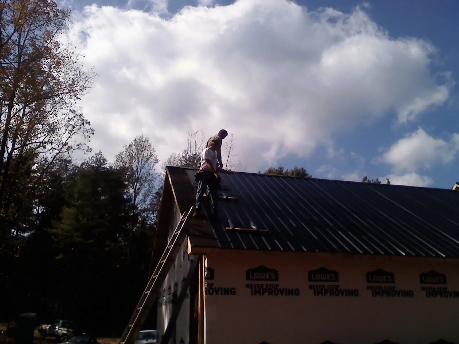 Roofer fastening dark metal panels high against a cloudy sky, from a Roof Inspection job in Arvada